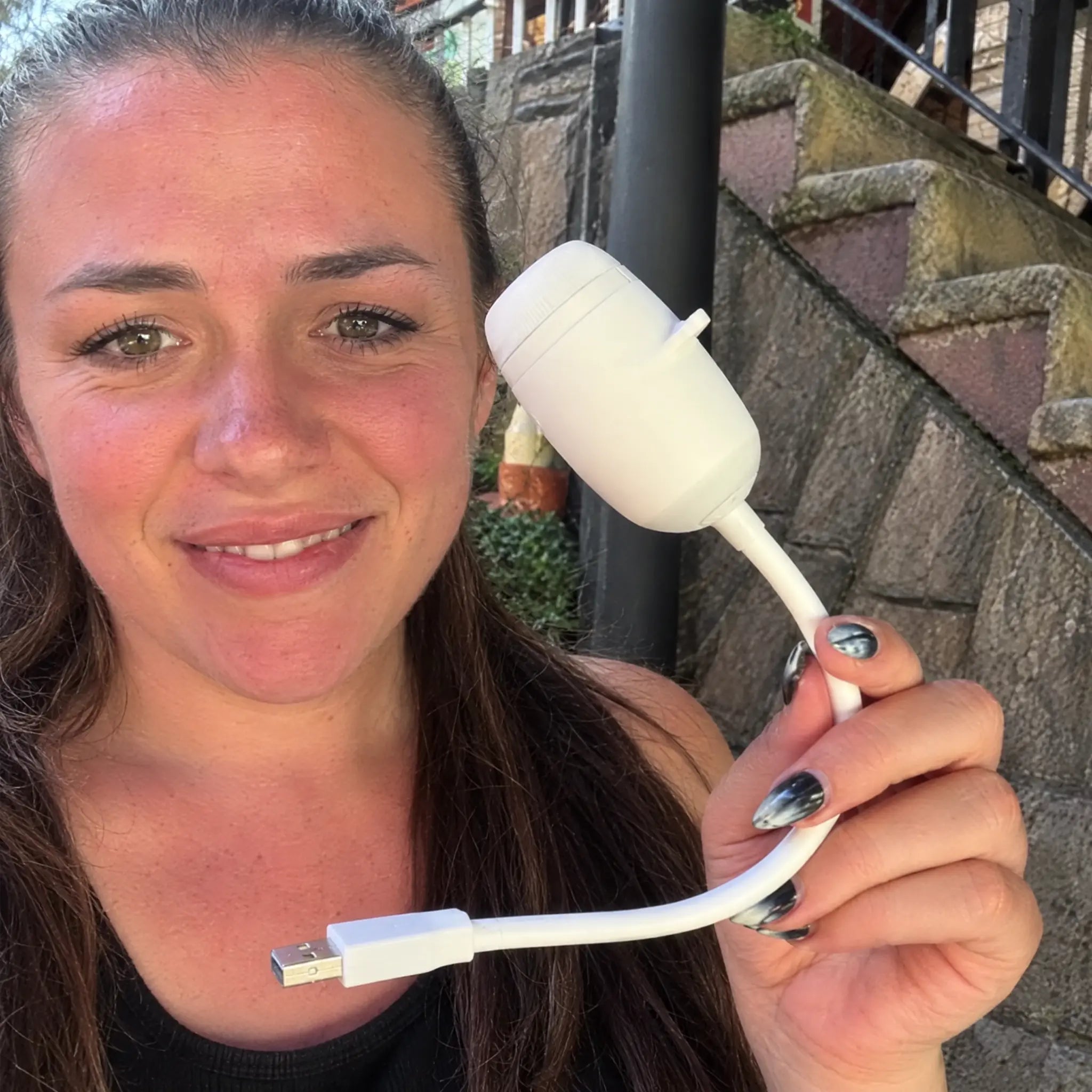 Young woman outdoors holding the projector and its USB cable